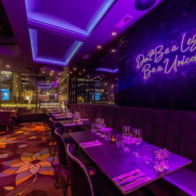 Seating area, banquette sofa with tableware on tables and chairs, purple neon wall sign.