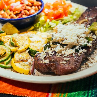 Grilled steak topped with fresh cheese, served with vegetables and beans.