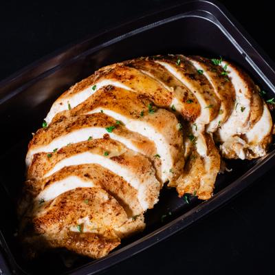 Chicken breast seasoned with herbs, served in a black takeout container.