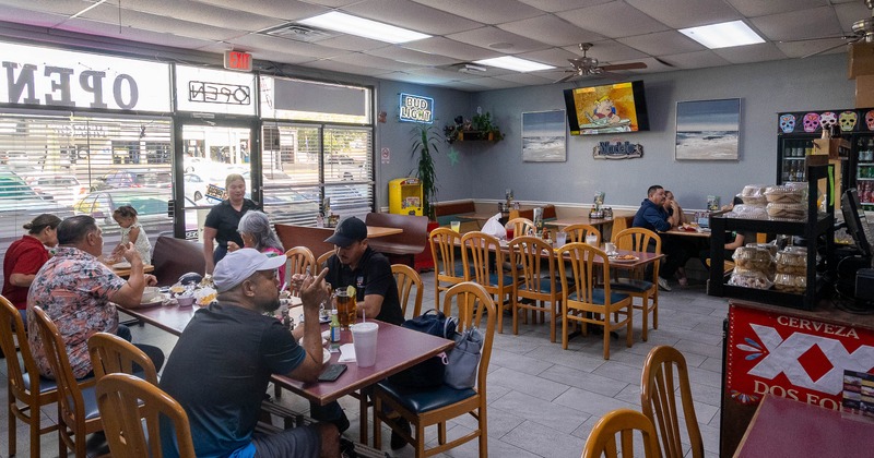 Diner tables, chairs, people, tv screen above