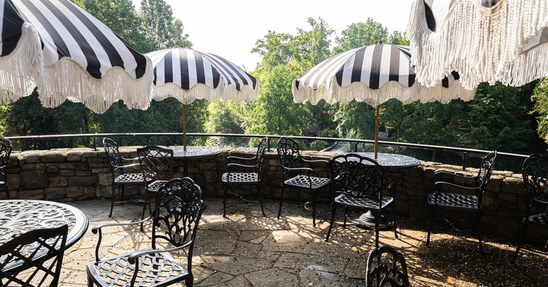 An outdoor patio with ornate black metal tables and chairs and black-and-white striped umbrellas
