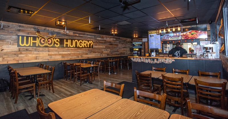 Interior with wooden décor featuring a neon sign reading "WHO’S HUNGRY?" and a front counter