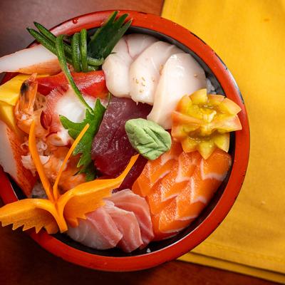 Assortment of fish on sushi rice bed, served in a bowl.