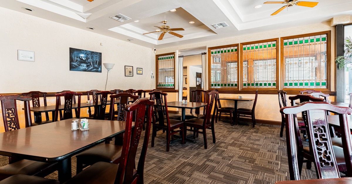 Interior of a restaurant featuring dark wooden tables and chairs, a ceiling fan, a wall lamp