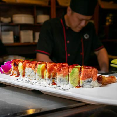 Big sushi roll plate sits on bar counter, Chef is working in the background.
