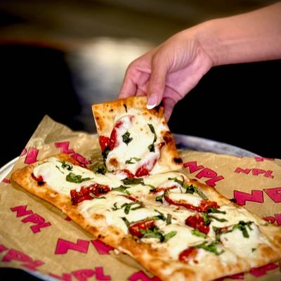 A hand lifting a slice of margherita flatbread.