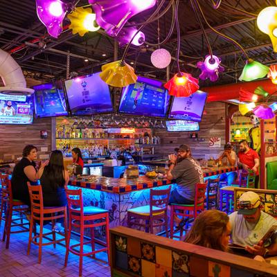 Colorful interior, customers are seated at a bar and booths, multiple TVs displaying sports.