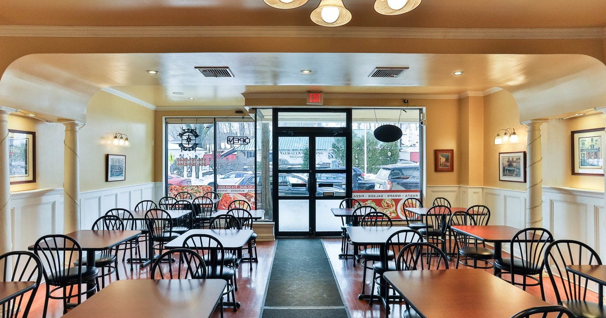Interior with multiple tables and chairs, beige walls and large glass windows and door.
