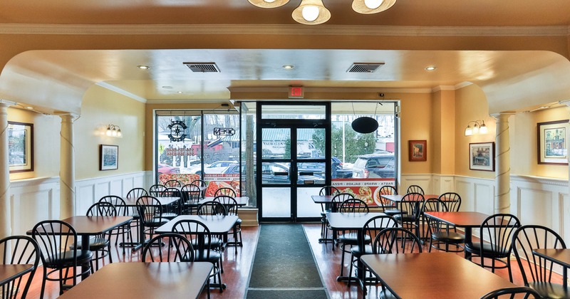 Interior with multiple tables and chairs, beige walls and large glass windows and door.