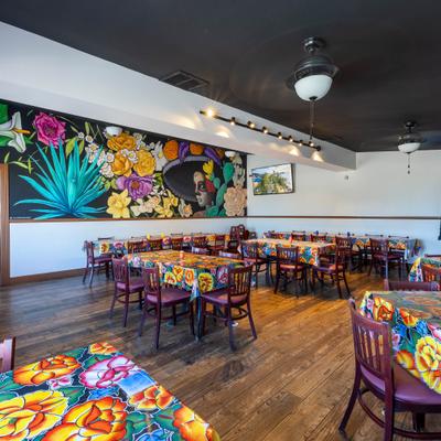 Mexican restaurant dining room featuring a large agave mural and colorful floral tablecloths.