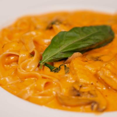 Orange Alfredo pasta dish garnished with basil leaf.