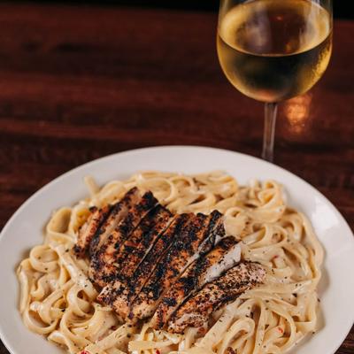Grilled chicken over creamy fettuccine pasta with a glass of white wine.