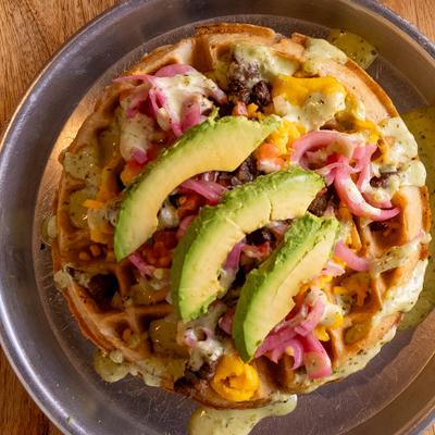 Carne asada waffle topped with avocado slices and pickled onions.