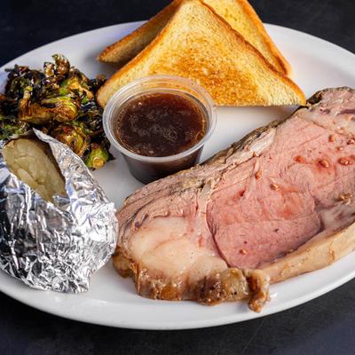 Prime Rib Eye Steak with baked potato, au jus, Brussels sprouts, and toast.