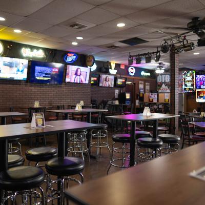 Interior with high-top seating, brick walls, neon signs, and TVs.