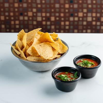 Bowl of tortilla chips served with two cups of salsa.