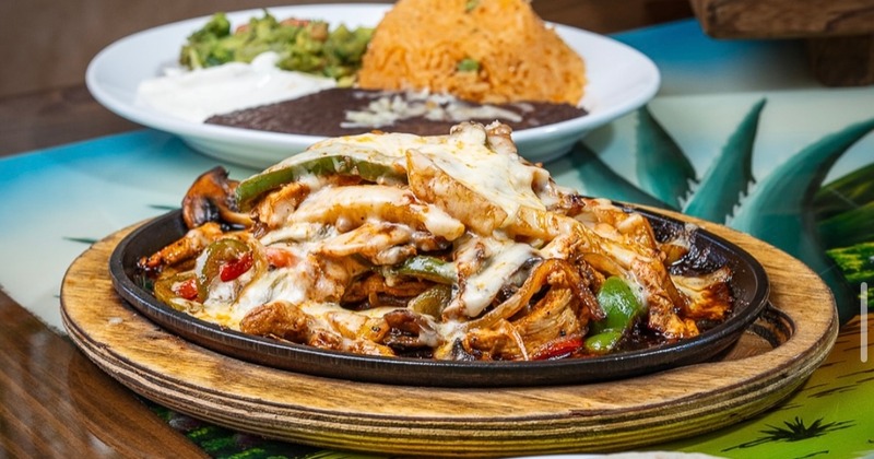 Chicken fajitas served with tortillas, rice, beans, sour cream, and guacamole