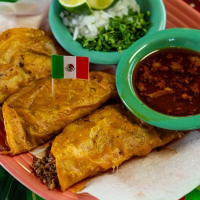 Birria tacos served with onion, cilantro, lime, and consomme.