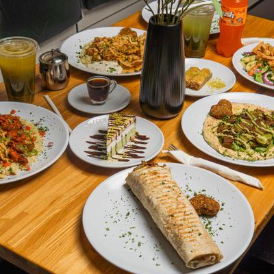 Variety of meals and desserts served on the table alionside condiments and drinks.