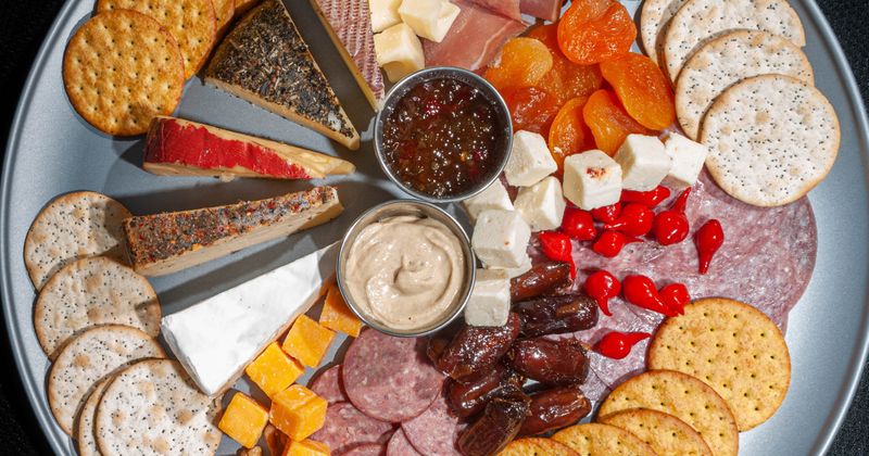 Overhead photo of meat and cheese tray with nuts, dried fruit, and crackers with a black backgroud..