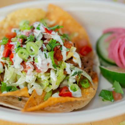 A vibrant taco on a corn tortilla topped with lettuce, tomatoes, green onions, and cilantro.
