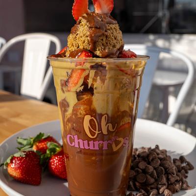 A dessert cup with layers of chocolate and caramel, topped with a scoop of dough and strawberry.