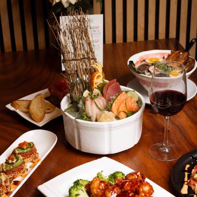 Variety of Japanese cuisine dishes on a dining table with a glass of red wine.