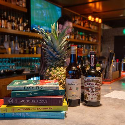 Liquor bottles with a pineapple and several cocktail books on the bar counter.