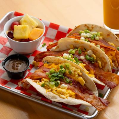 Breakfast tacos with a dip and small bowl of fresh fruit.