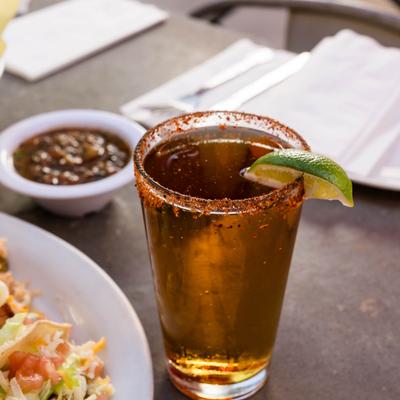 A glass of beer with tajin rim and a lime wedge.