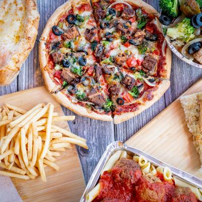 A variety of dishes on a wooden table, including, pizza, pasta, fries, salads, and garlic bread.