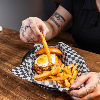 Person having a burger topped with a fried egg and a side of fries.