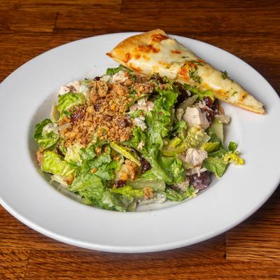 Mixed greens salad with chicken, breadcrumbs, cranberries and a slice of cheesy flatbread.
