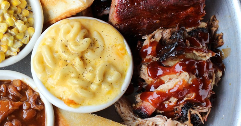 A close up of BBQ meat with mac and cheese, cream corn, toast, and baked beans