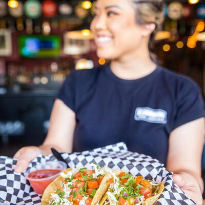 Smiling Staff woman serving basket of cheese nachos  with housemade salsa