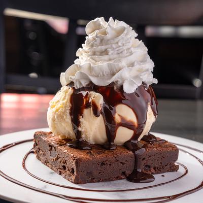 Brownie topped with ice cream chocolate and whipped cream.