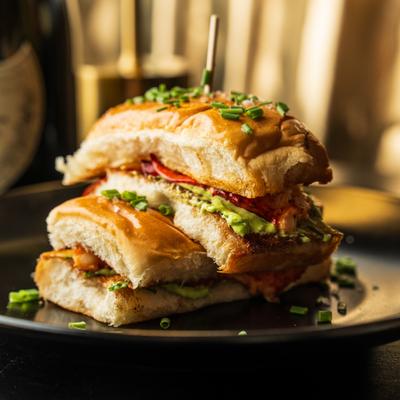 Stacked chicken pesto sandwich with chive garnish on a plate.
