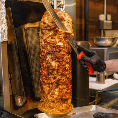 Chicken shawarma being sliced from a vertical rotisserie spit.