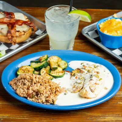 Tilapia fillet topped with white sauce, served with rice and veggies, alongside a drink.