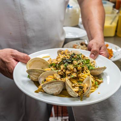 Chef holding a plate of clam linguine pasta.