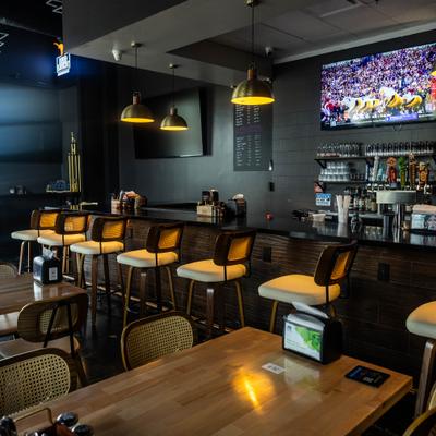 Bar area with a counter, stools, hanging lights and television screen on the wall.