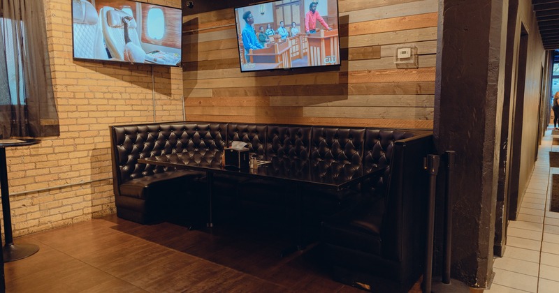 Interior, button tufted leather booth seating in a corner with TVs on walls