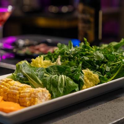 Platter of fresh vegetables, including bok choy and sweet potato and corn on a cob.
