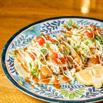 Fish tacos topped with a creamy sauce, served with a lemon wedge.