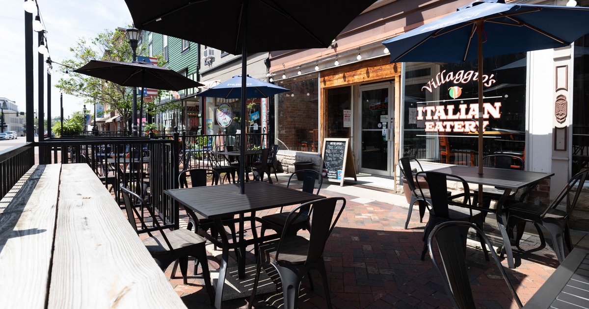 Outdoor seating area with tables, chairs, and umbrellas on a brick sidewalk
