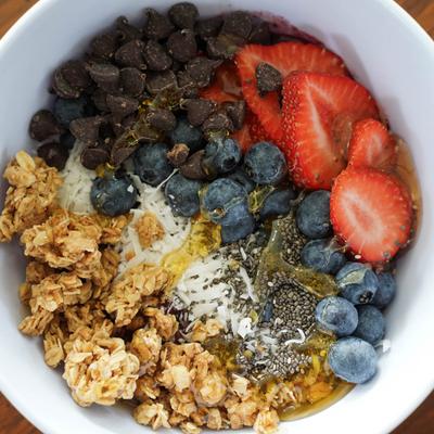 A bowl of granola and yoghurt with blueberries, strawberries, chia seeds, and chocolate chips.