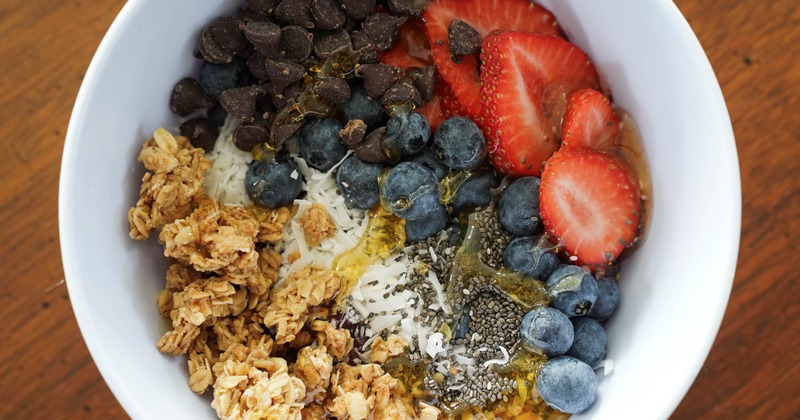 A bowl of granola and yoghurt with blueberries, strawberries, chia seeds, and chocolate chips