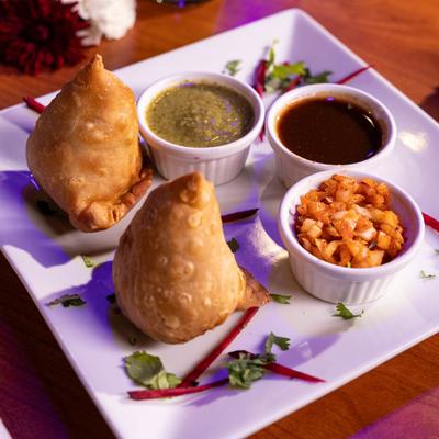 Two samosas with dipping sauces.