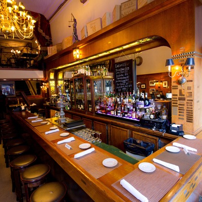 Elegant bar with stools, menu board, liquor bottles, and a chandelier.