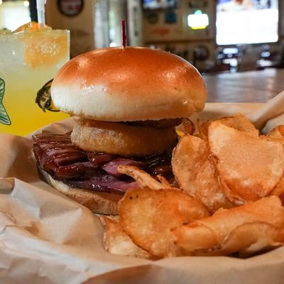 Smoked Brisket Sandwich topped with a onion ring and served with chips.